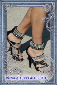 A beautiful and seductive female is standing, showing off her seductive foot while donning a pair of black slippers.
