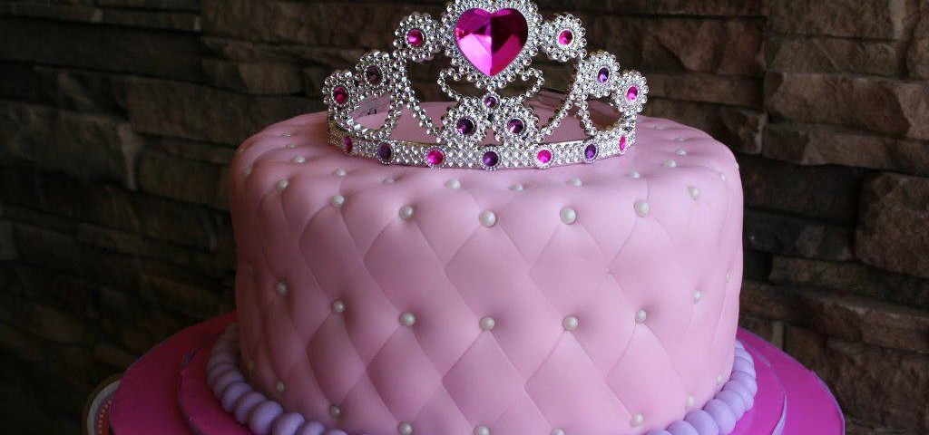 A lovely cake with pink frosting and jewellery for a princess's hair is displayed.