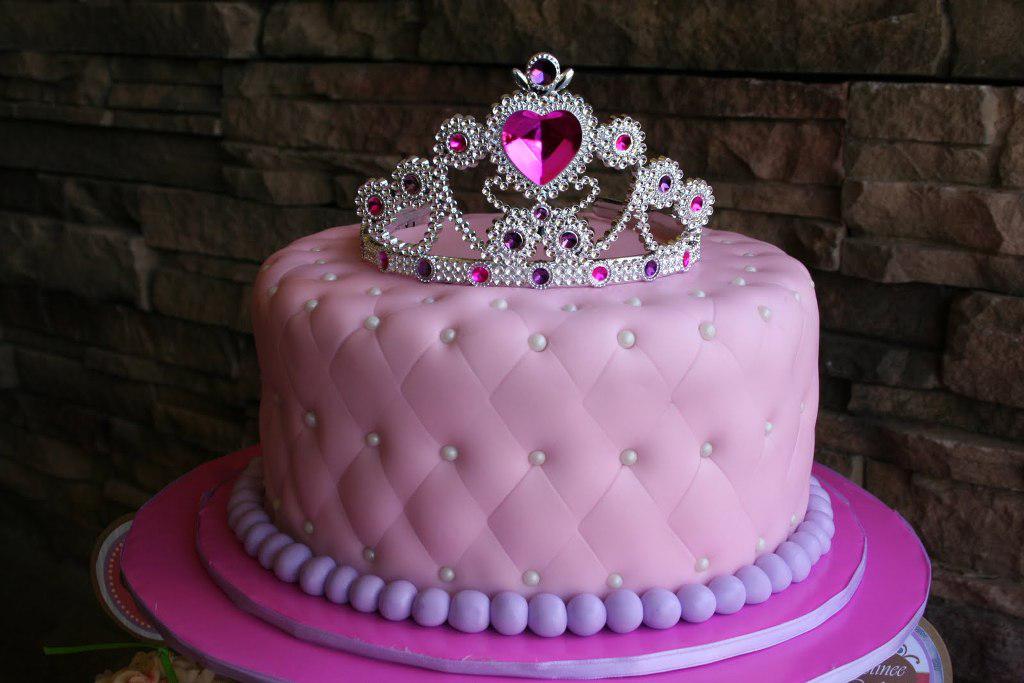 A lovely cake with pink frosting and jewellery for a princess's hair is displayed.