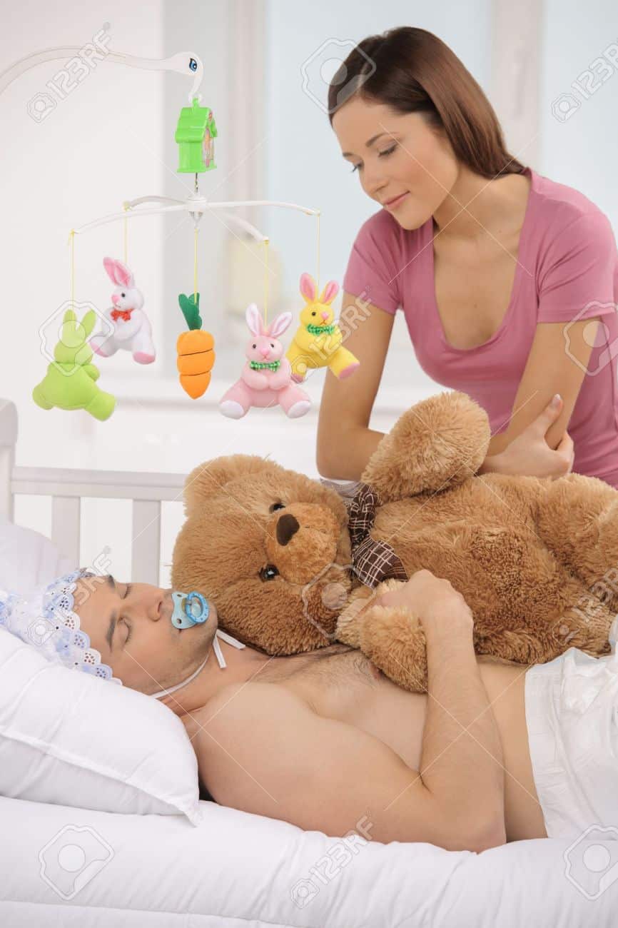 A sexy mother is laying in bed while a sexy woman is sitting in bed and lovingly observing the boy.