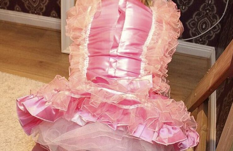 A diaper boy is seated on the ground, showing off his back while donning the pink sexy drees.